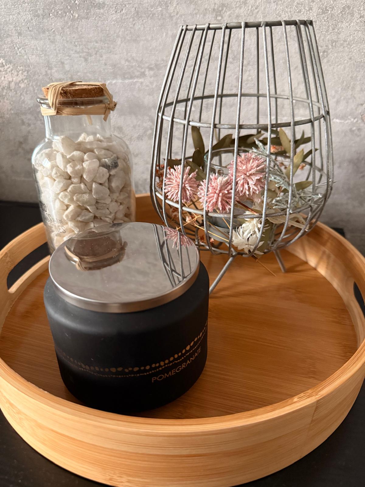 Tablett mit schwarzer Kerze, Glasflasche mit Steinen und Blumendeko im Metallkorb