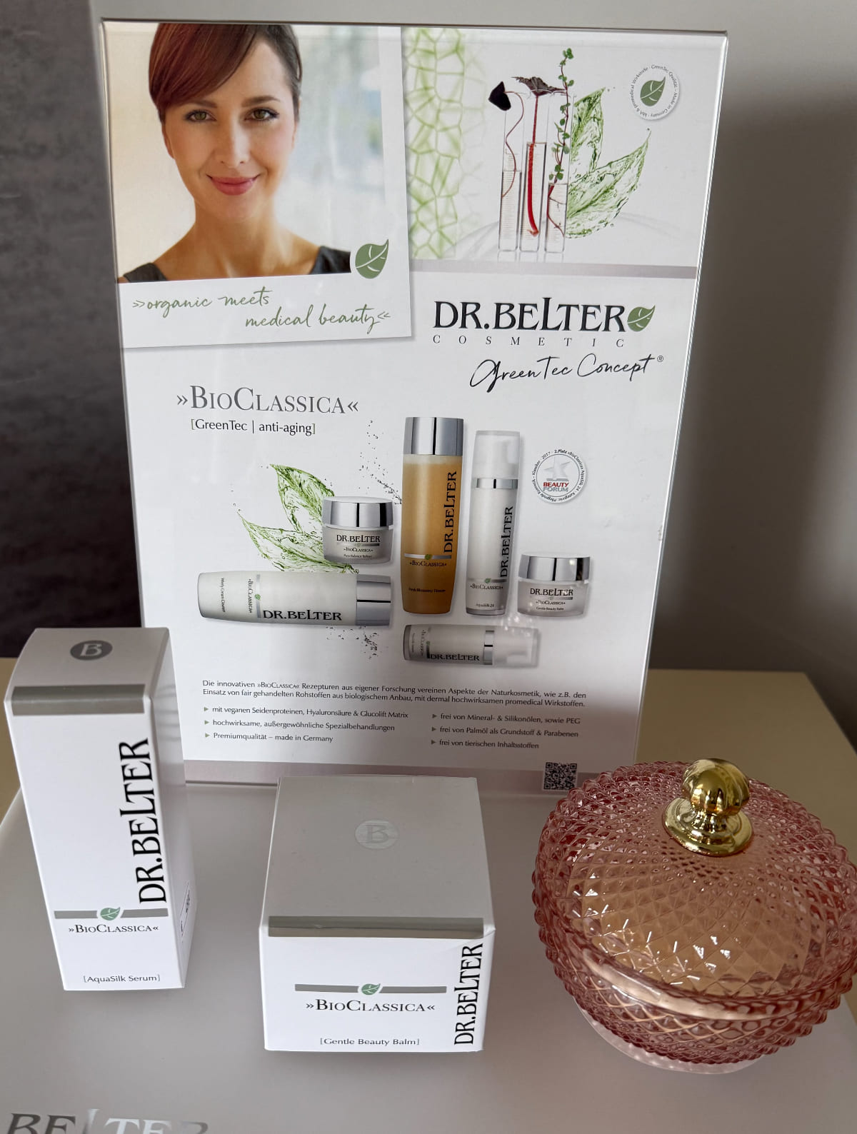 Eine Werbeanzeige mit Dr. Belter Kosmetikprodukten, darunter elegante Flaschen und ein rosa Glasflakon